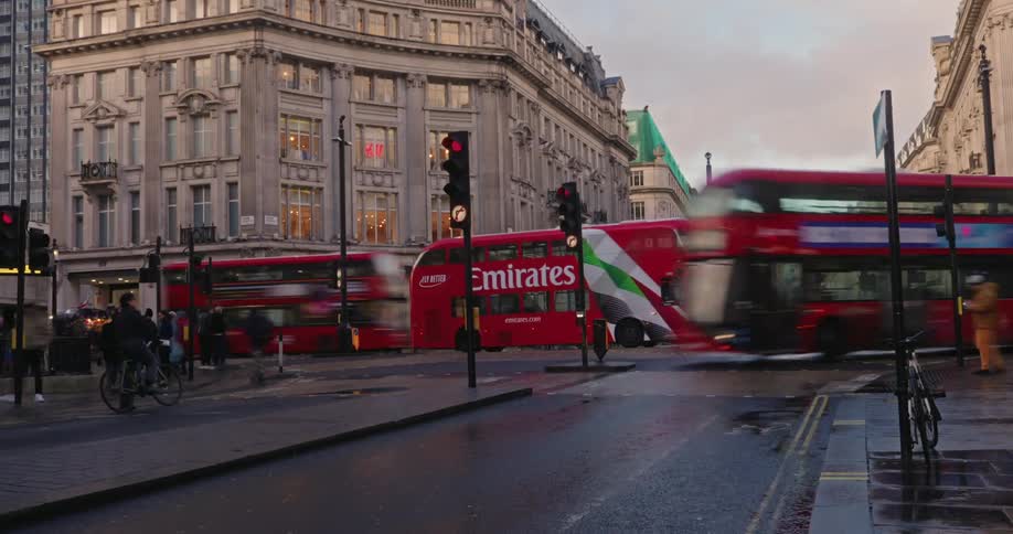 People crossing oxford street in london as cars and double decker buses travel past