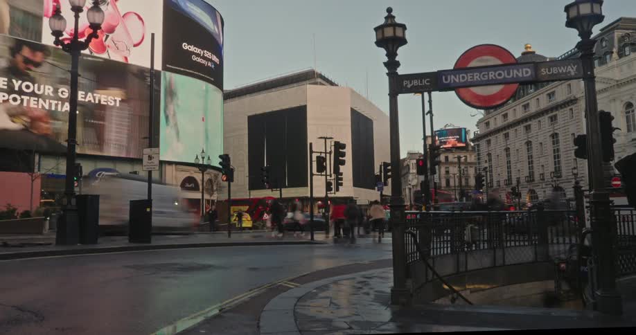 Red doubledecker buses and pedestrians pass by the iconic curved advertising screens and historic buildings of piccadilly circus in london under an overcast sky