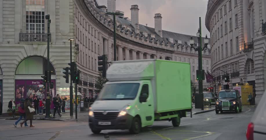 A busy urban street in london with a mix of red doubledecker buses taxis and pedestrians framed by historic and modern buildings