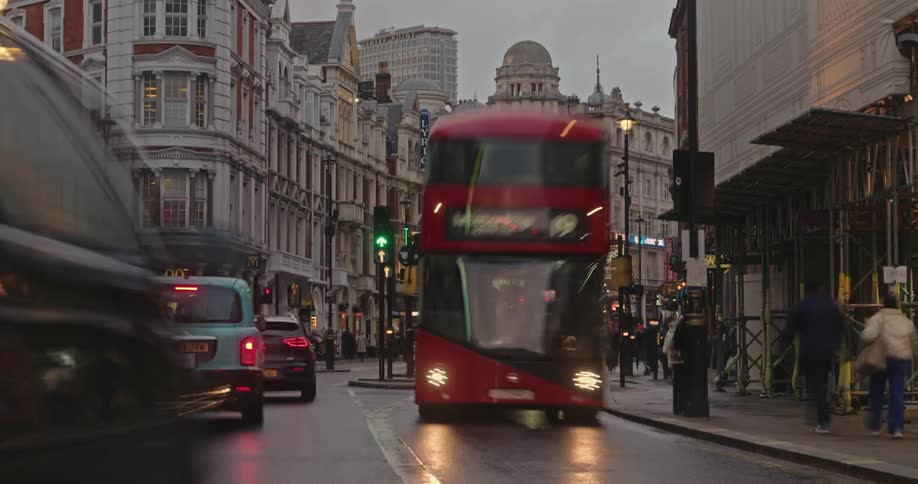 A busy urban street in london with a mix of red doubledecker buses taxis and pedestrians framed by historic and modern buildings