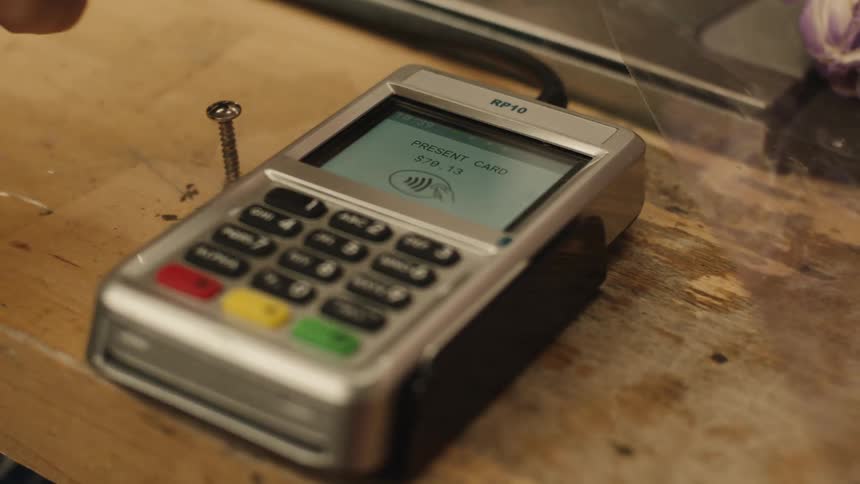 Person holds a red card near a payment terminal on a wooden counter
