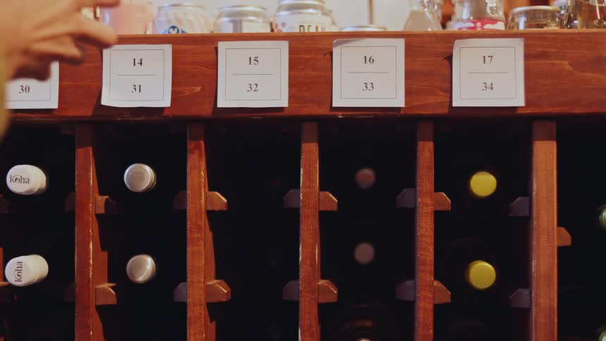 Person removes and places a bottle of wine from a numbered wooden rack
