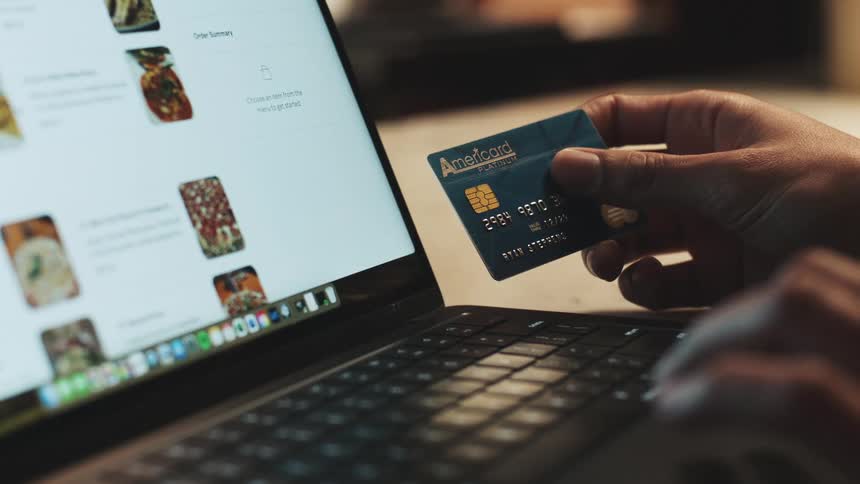 Person holds a credit card while using a laptop to shop online
