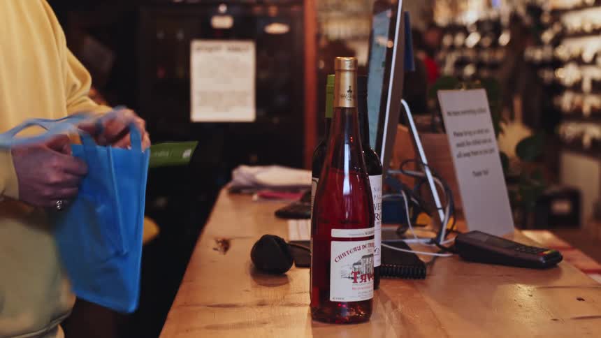 Salesperson scans a bottle of wine on the counter with a barcode reader and then places it in a blue bag