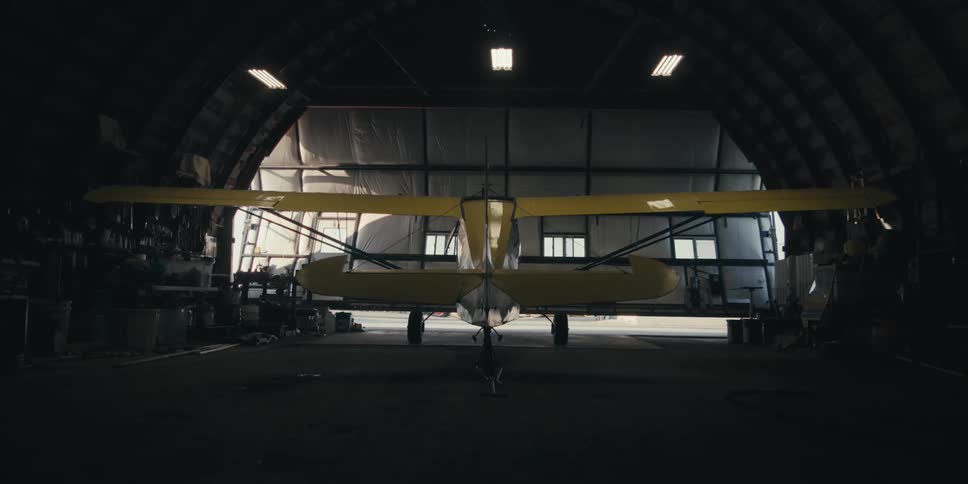 A yellow single engine plane parked in a hangar as the door closes