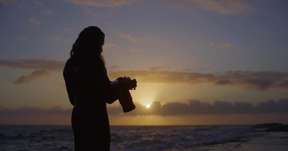 Silhouette man looking at a camera standing near the ocean at sunrise