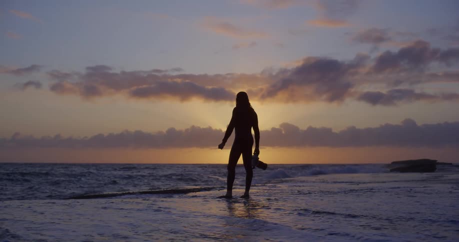 Male photographer silhouetted against a red sky stands on the coast holding a camera