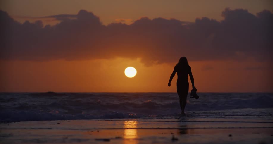 Male photographer running towards the surf while carrying a camera and wearing a wet suit at sunset turns slightly