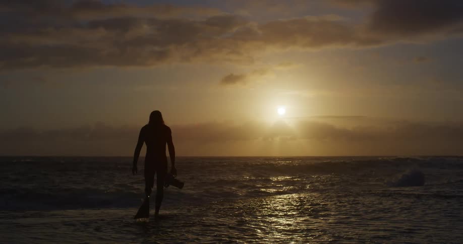 Silhouette man walking in the ocean at dawn