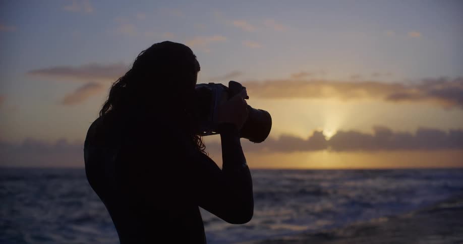 Male photographer standing on the coast against a red horizon takes a photograph
