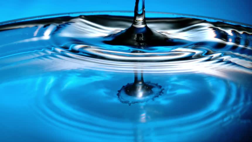 A droplet of water falls and splashes into the surface of crystal clear water