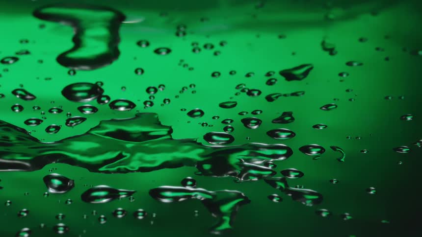 Drop falling on a surface with water and spreading against the greenish background