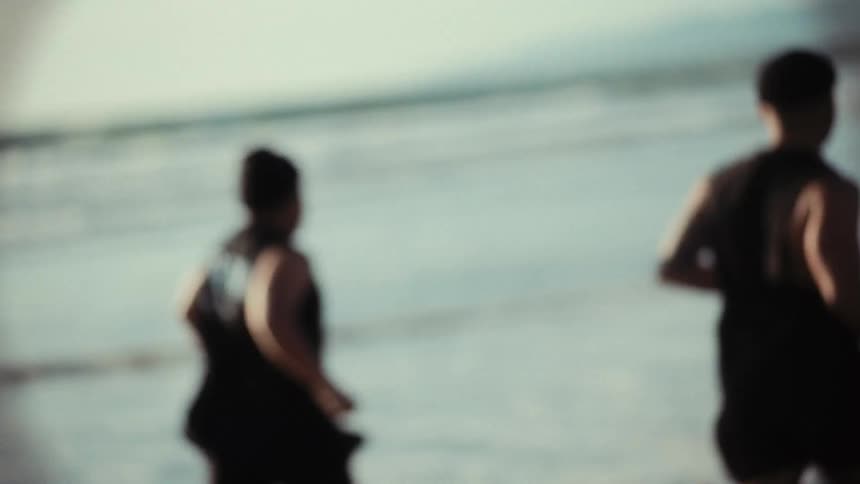 Two male friends wearing black beanies race along the beach at sunrise startling seagulls into flight as the waves roll ashore