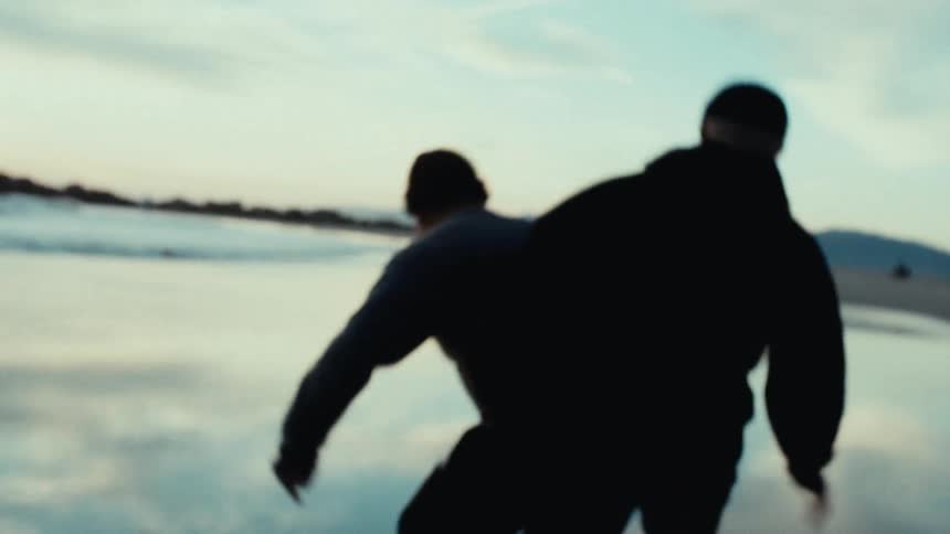 Two men are playing soccer on the beach