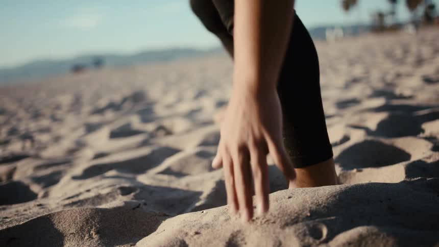 A man runs sideways in the beach sand back and forth and touches the ground each time