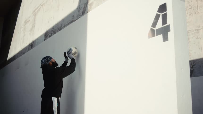 A man standing hitting a ball at a white wall with the number four on it