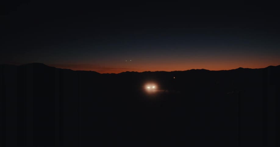 Headlights shine brightly as a car drives through the rural countryside at night