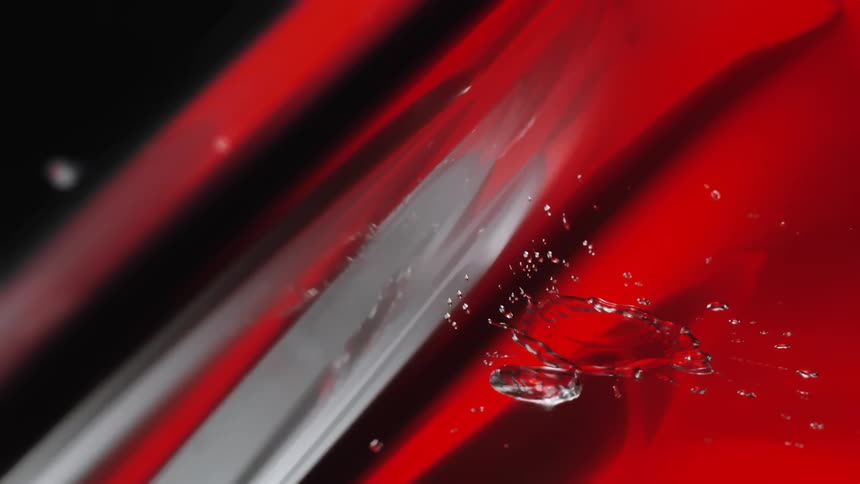 Water droplets scatter across a shiny red surface with abstract light streaks and reflections