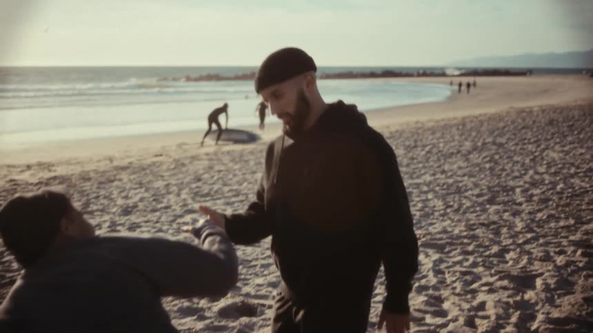 Two hispanic men are standing on a beach while taking off their sweatshirts