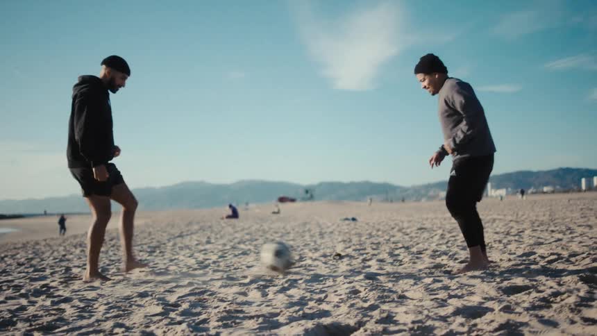 Two men on the beach sand playing soccer passing the ball to each other
