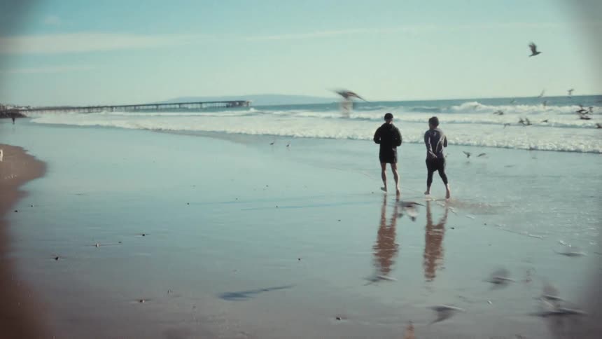 Two men running on the beach with birds flying around