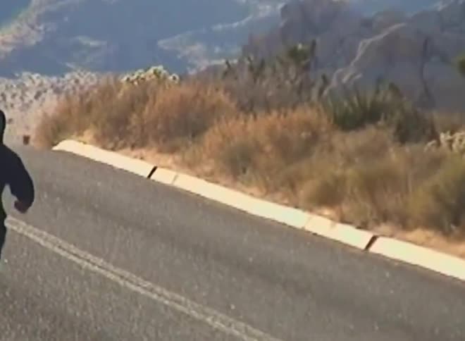 A runner in dark clothing is seen jogging away down a road amidst a desert landscape with joshua trees