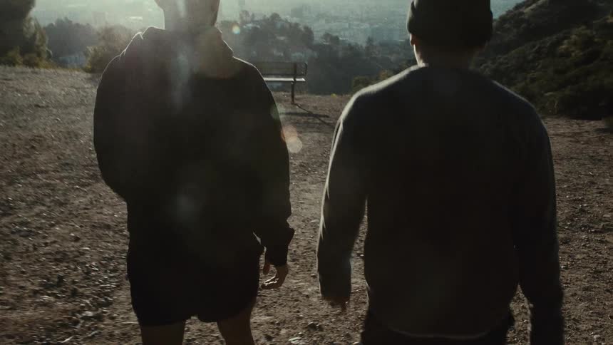 Two men are walking along a dirt path on top of a hill on a sunny day