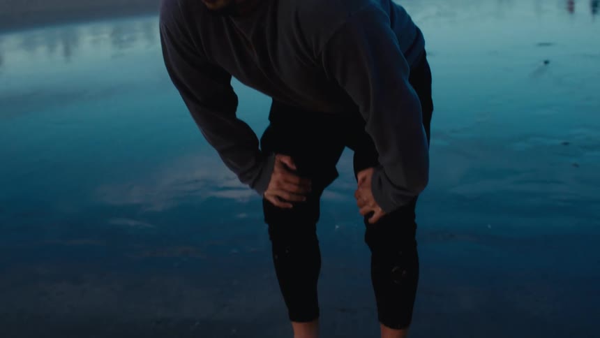 A man is leaning over resting on the beach