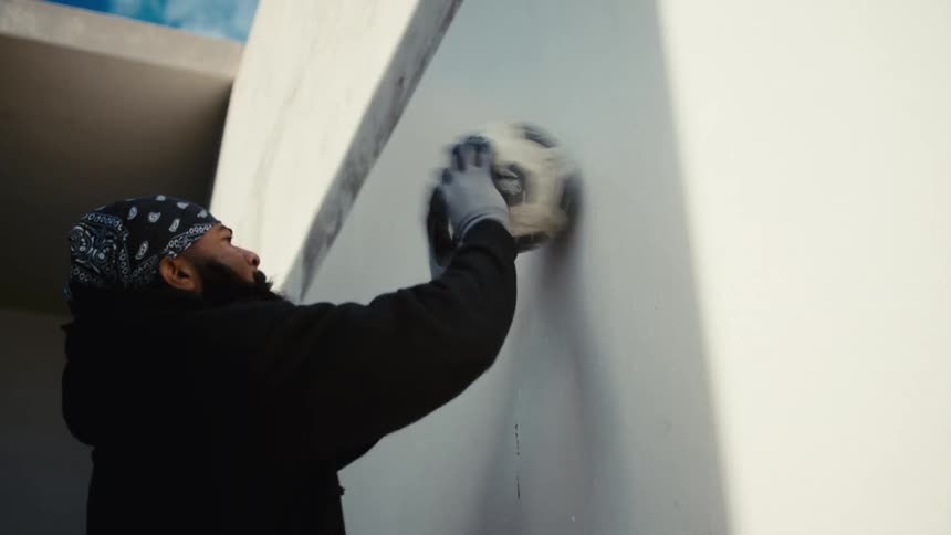 Man with a bandana on his head bouncing a ball against a wall