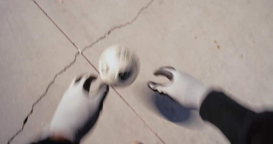 A pair of gloved hands spins a small white soccer ball over a concrete surface