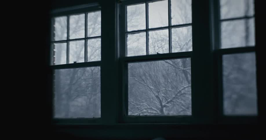 A window looks out onto a snow covered scene the room shrouded in darkness
