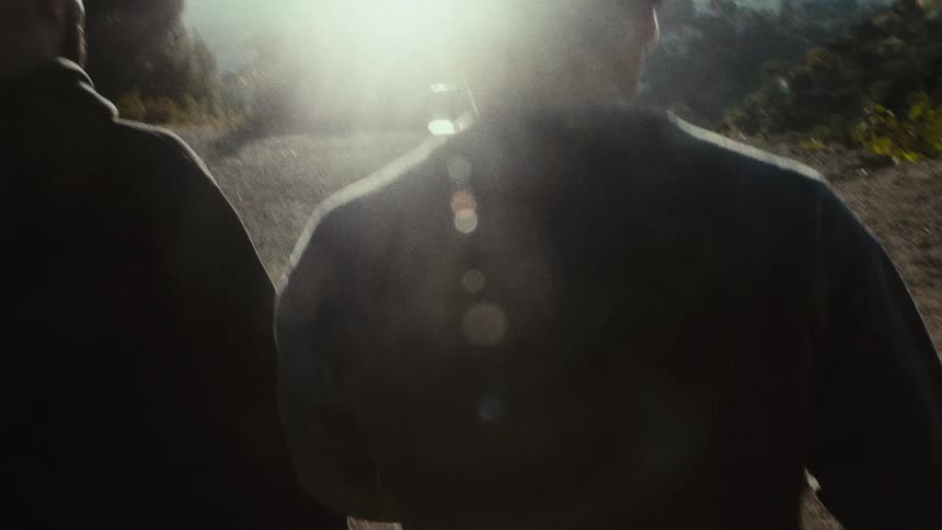 Two men walk towards a scenic overlook with a city skyline in the distance