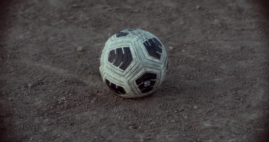 Person kicks a soccer ball sitting on bare dirt during the daytime