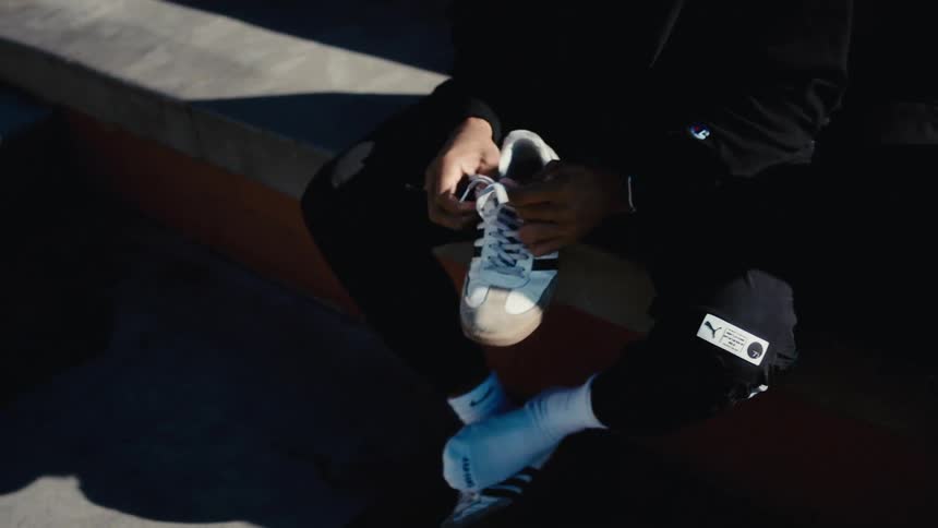 Man sitting in a row in stadium seating during the daytime puts on sneakers