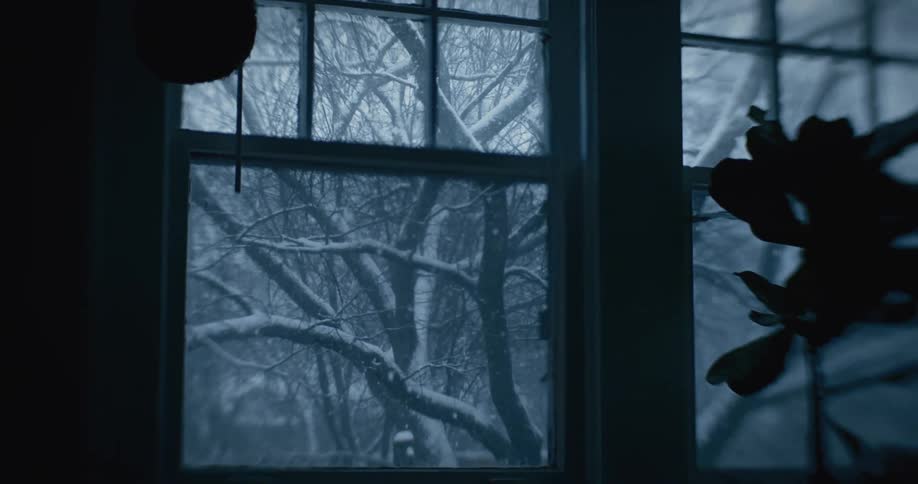 A bedroom window with a view of the outside where a blizzard is falling
