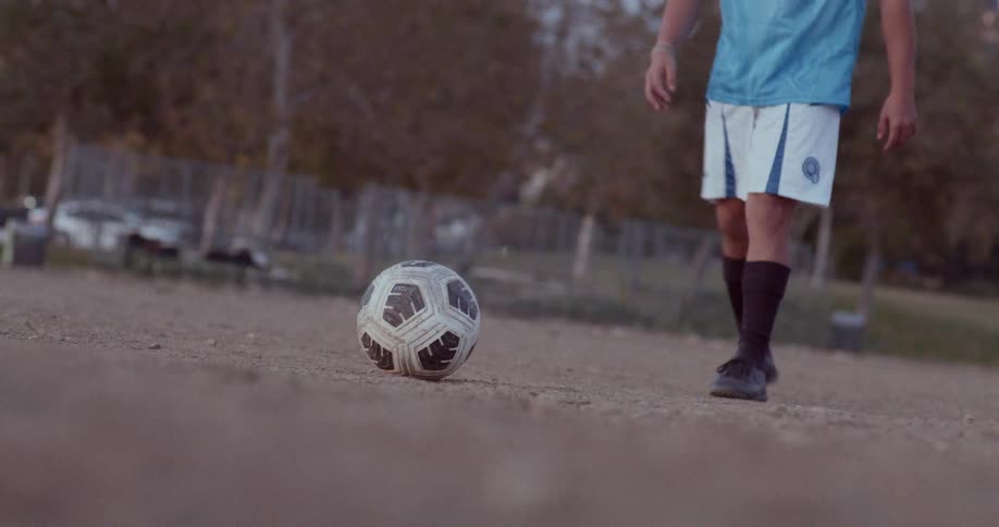 Man places a soccer ball on the ground in the park on an autumn day then runs forward and kicks it