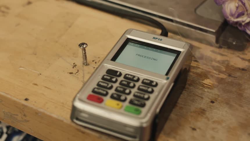 Woman makes a contactless payment at a shop with a wooden counter