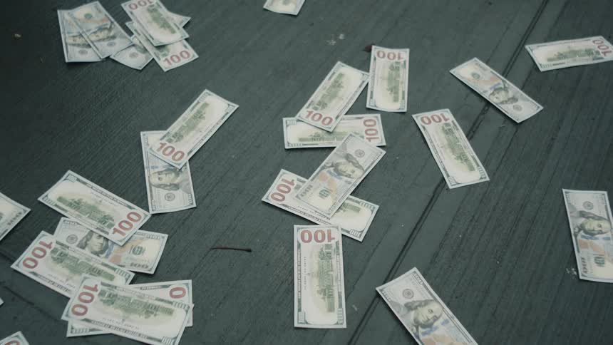Hundred dollar bill falls onto a floor scattered with hundred dollar bills