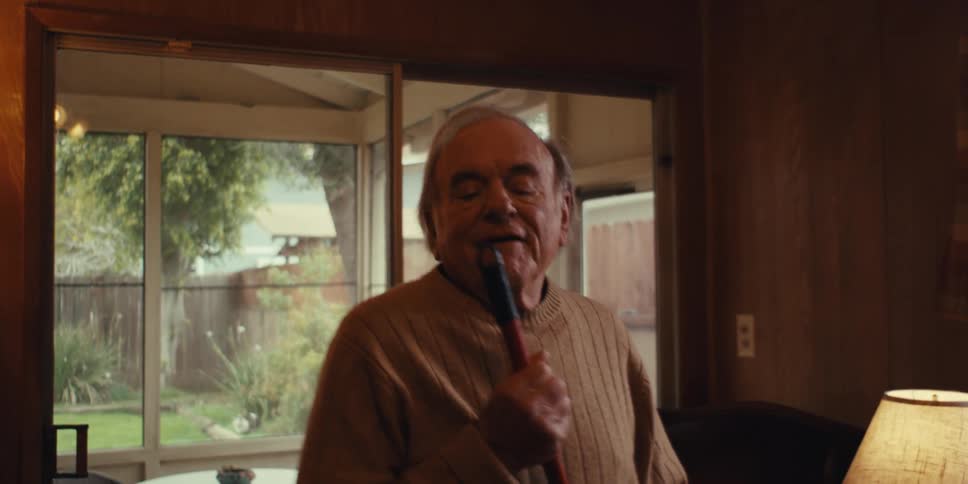 Elderly man sings and dances while cleaning the floor at home in his living room