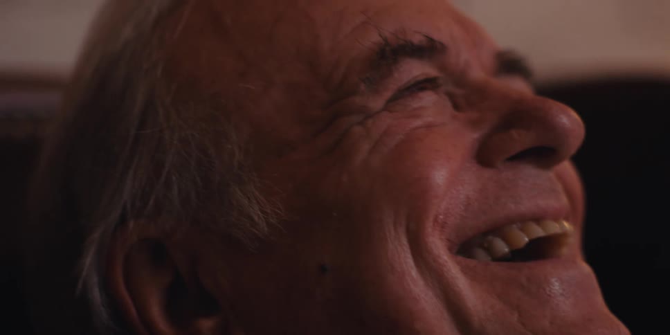 Elderly man laughing while holding and interacting with a smartphone