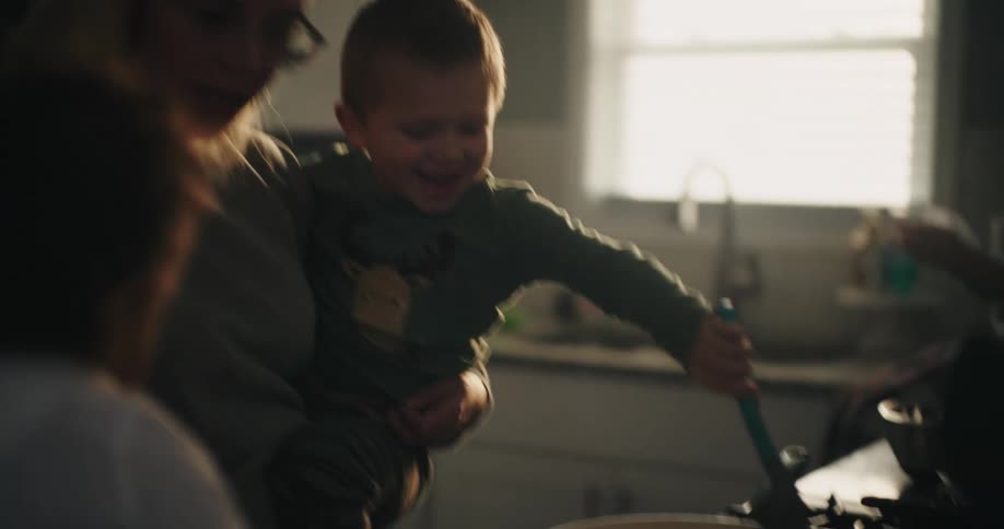 Mother with a small child on her lap cooking and two other children around in the kitchen
