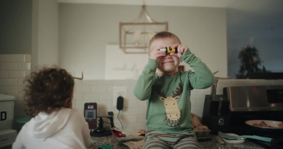 The face of a little blond boy in a green shirt who is sitting and fiddling with a small glass container with a strip