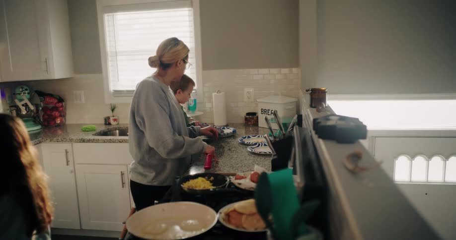 A mother and her children are preparing food on the kitchen counter in the morning