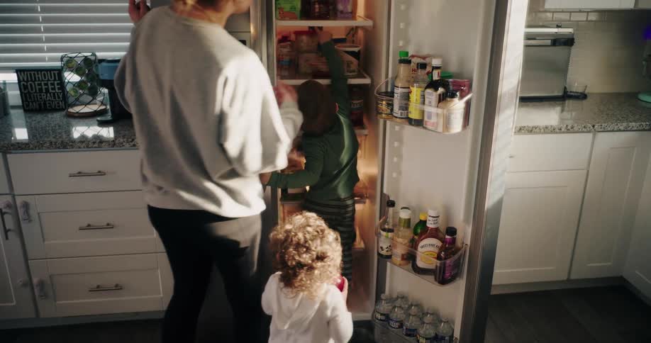 Child at the refrigerator door with mother taking food