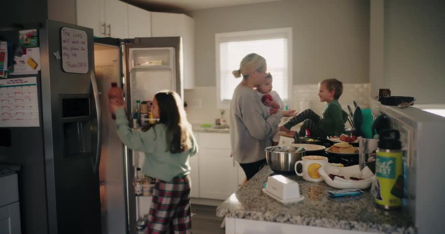 Woman in the kitchen with three children and one of them taking a product from the refrigerator