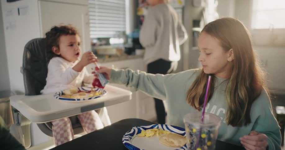 Girl opens a snack for her younger sister while their family eats at home