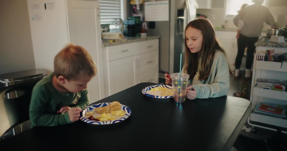 Mother holding a baby on her lap and placing a plate of pancakes for her other two children who are sitting at the table