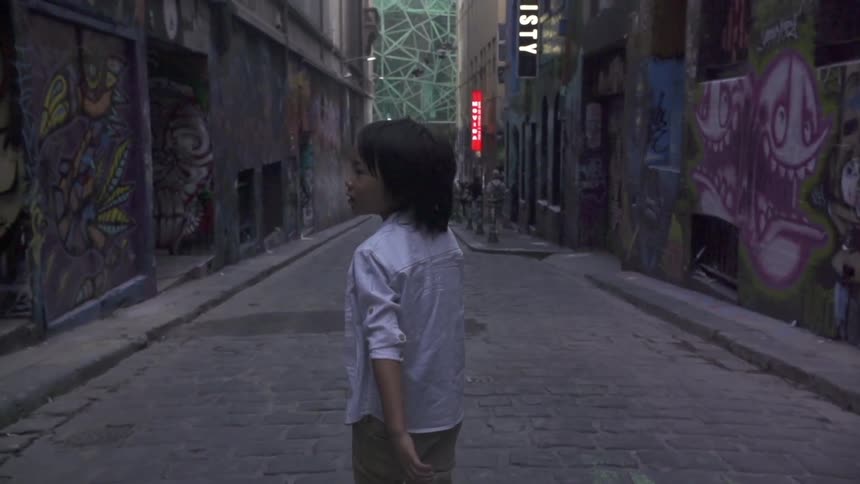A boy walks on a city street with graffitied buildings all around
