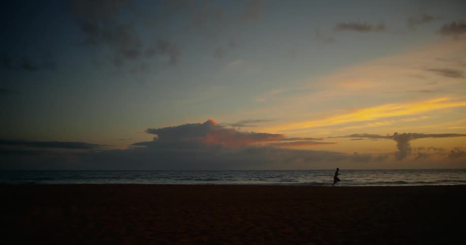 A person running on the sand of a beach on a morning with an orange sky