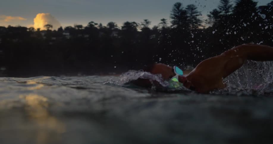 Man is swimming in a body of water during sunset